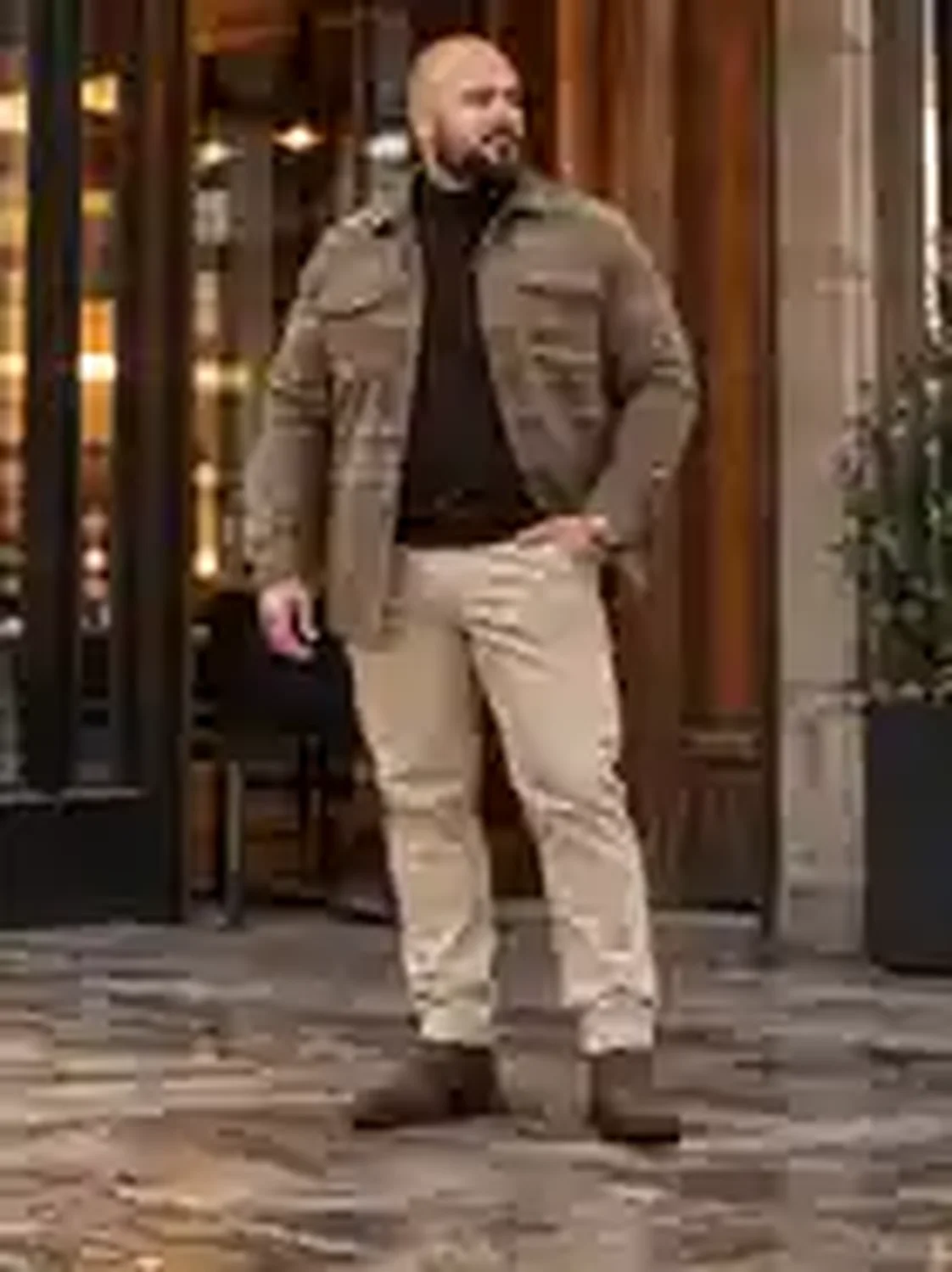 Mann mit braunem Karo-Overshirt, dunkelbraunem Rollkragen, sandfarbener Hose und braunen Chelsea Boots vor einem Café.